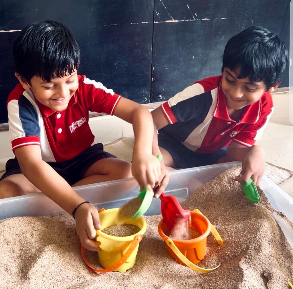 Two boys playing with sand using buckets and shovels indoors at one of the best preschools in Kukatpally.