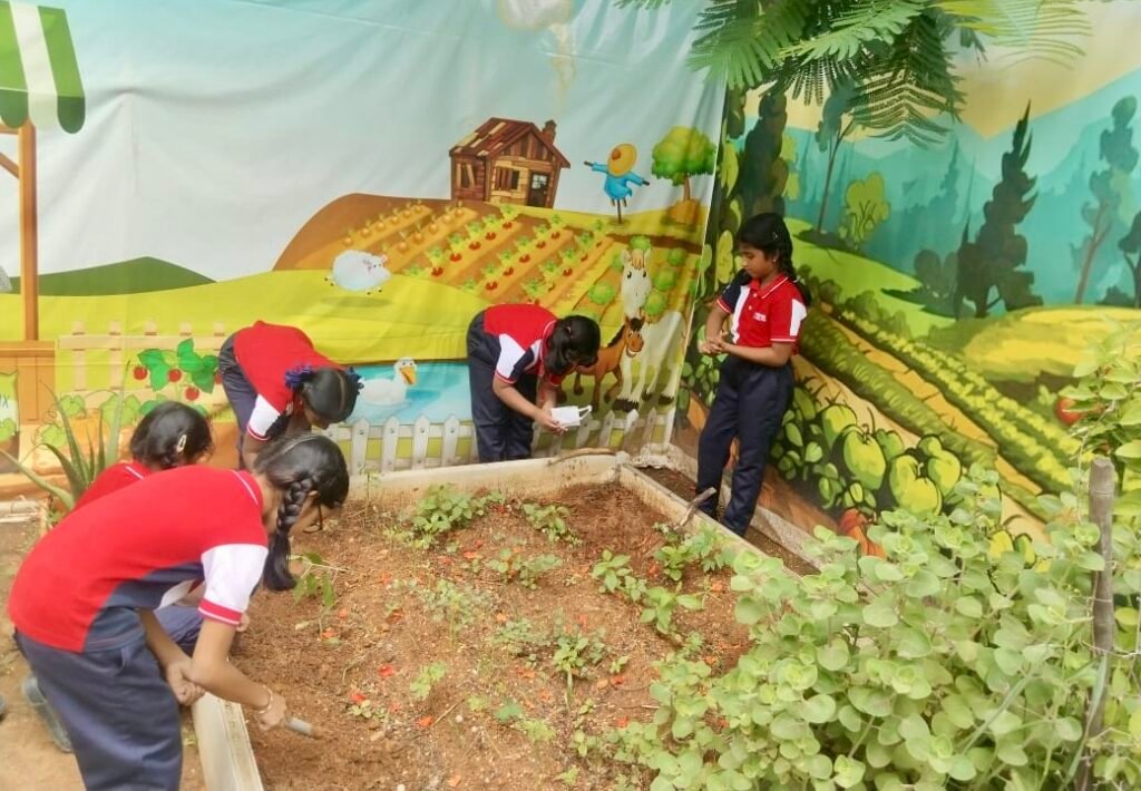 Girls planting seeds in garden bed with farm mural at best preschool in Miyapur.